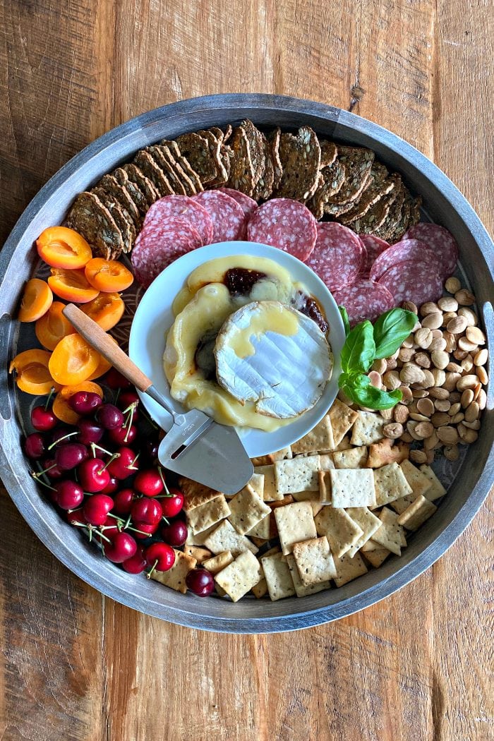 beautiful cheese board with brie, crackers, nuts, apricot halves, and bright red cherries