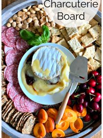 a brie cheese board with salami, crackers, apricots, cherries, and nuts