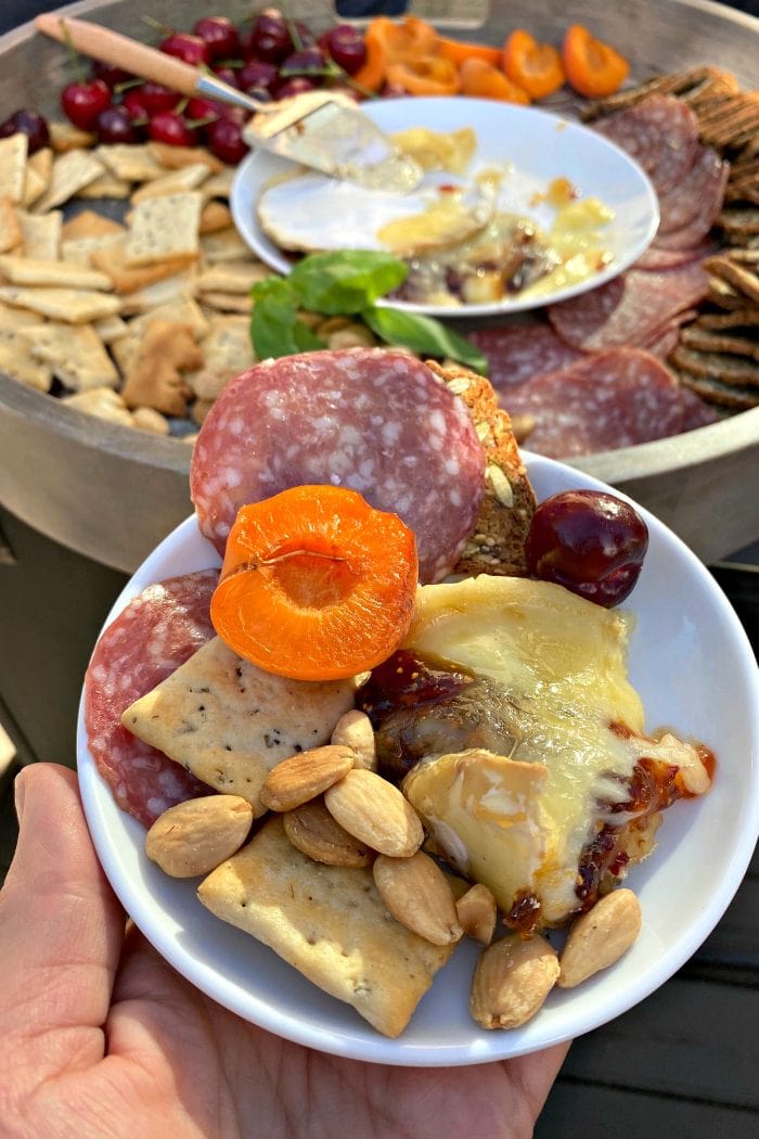 small plate with a wedge of brie cheese, salami, crackers, and apricot half