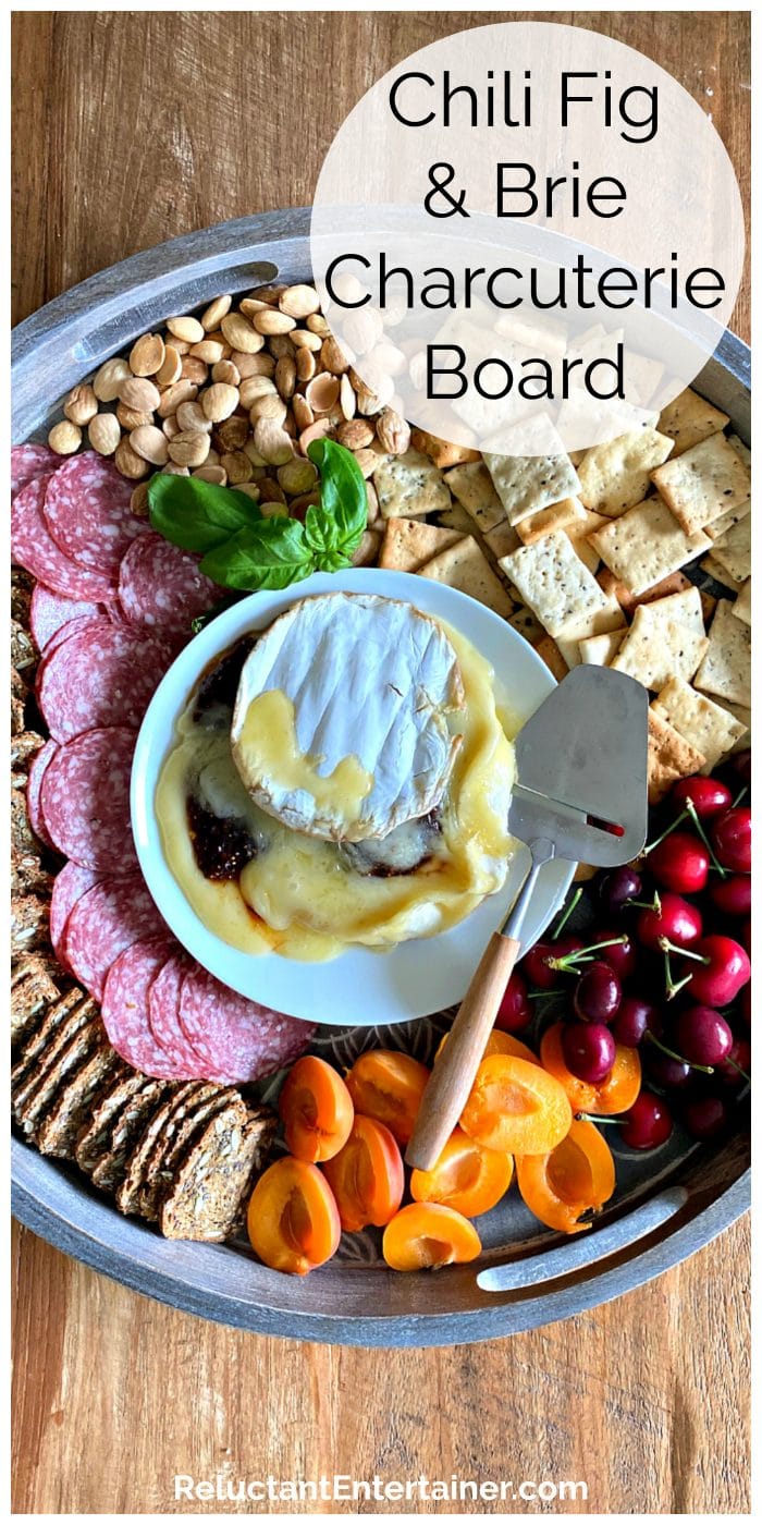 a brie cheese board with salami, crackers, apricots, cherries, and nuts