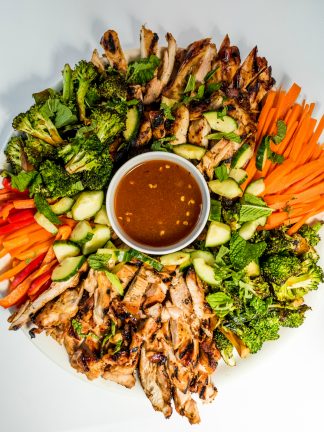 a platter of chicken thighs cut into strips with veggies, and dip in a bowl in the center