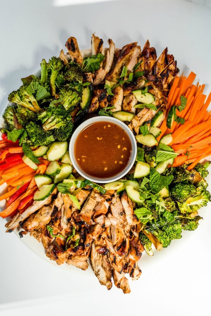 a platter of chicken thighs cut into strips with veggies, and dip in a bowl in the center