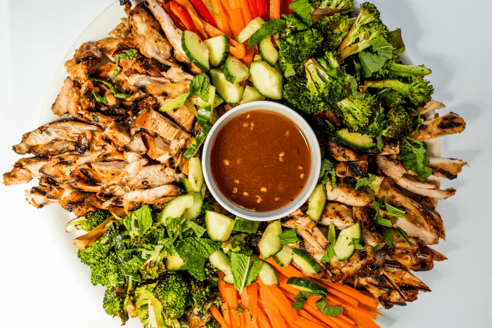 colorful platter of veggies and grilled chicken thighs with a dipping sauce in the center