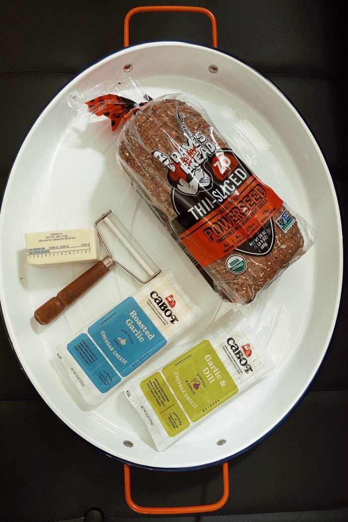 large white oval serving tray with a loaf of bread, cheese slicer, cube of butter, and 2 kinds of cheese