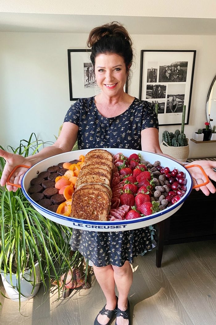 woman holidng a large white tray with grilled cheese sandwiches and fresh fruit