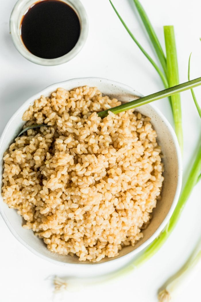 a bowl of brown rice, with green serving spoon, and a small bowl of soy sauce