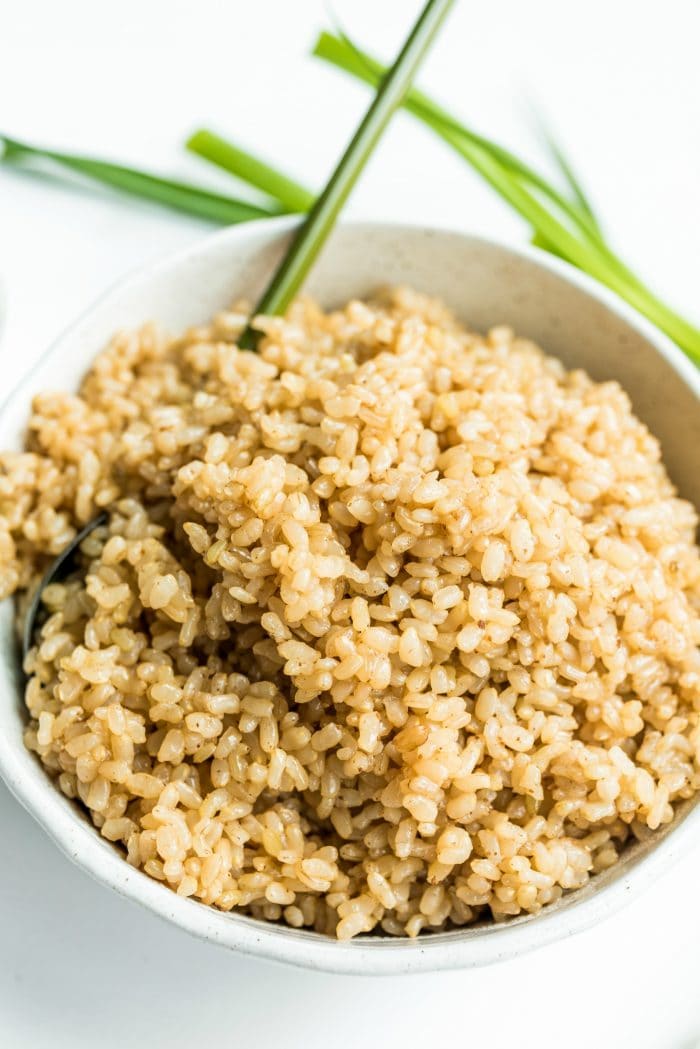 close up of cooked brown rice in a white bowl with a green spoon