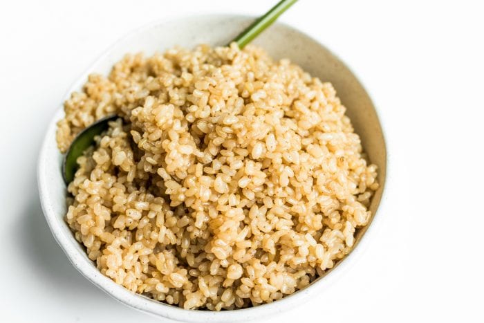 a bowl of cooked brown rice with a green spoon