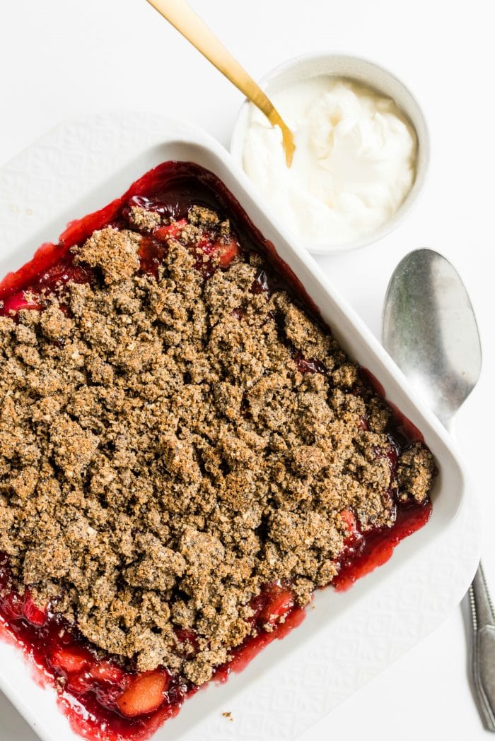 whipped cream in a small bowl with strawberry rhubarb crisp in white baking dish