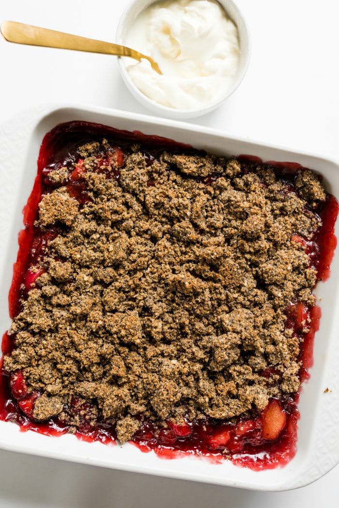 square pan of strawberry rhubarb crisp with a small bowl of whipped cream