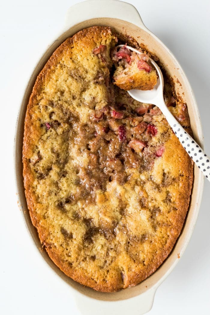 oval baking dish of rhubarb strawberry cobbler hot out of the oven with a polka dot spoon