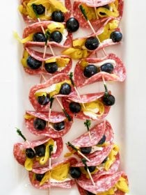 a white platter of salami pepperoncini rollups