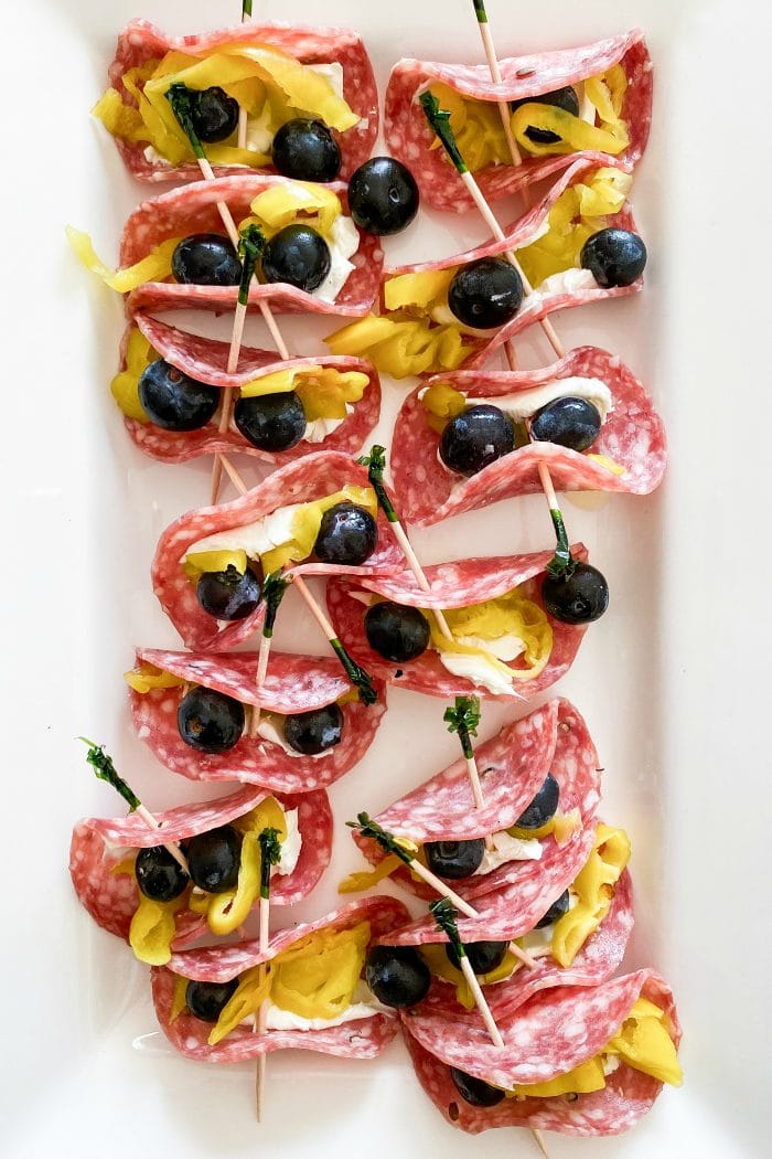 a white platter of salami pepperoncini rollups