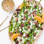 Shaved Fennel Asparagus Salad on an oblong platter wth a small bowl of orange dressing and gold serving tongs