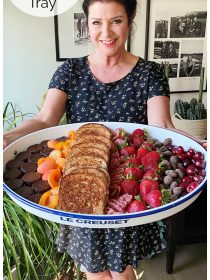 woman holding a large white tray filled with grilled cheese sandwiches and fresh fruit