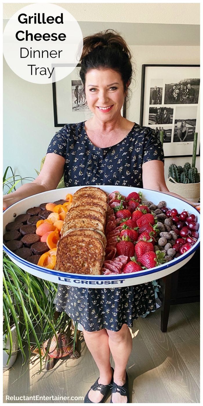 woman holding a large white tray filled with grilled cheese sandwiches and fresh fruit