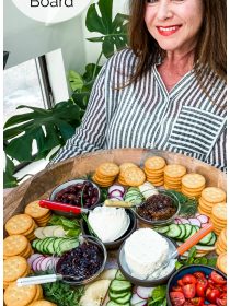 lady in black and white striped blouse holding a large round tray of Ritz crackers, cheese, veggies, jams