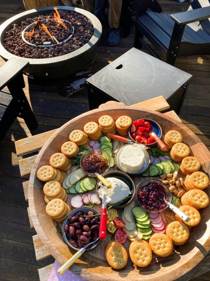 round tray of Ritz crackers with veggies and cheese by an outdoor fire