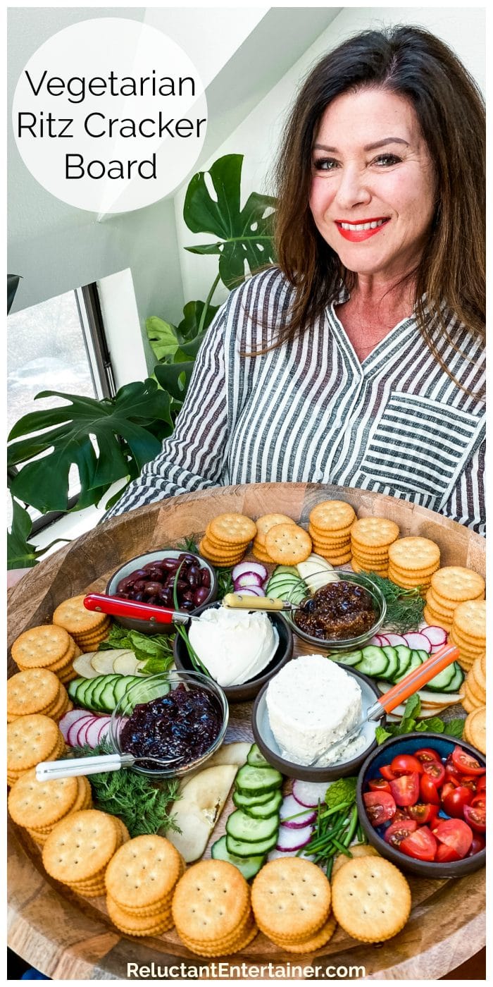 lady in black and white striped blouse holding a large round tray of Ritz crackers, cheese, veggies, jams