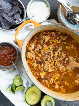 oval pot of chicken tortilla soup with black beans, corn, served with salsa, sour cream, lime, tortilla chips