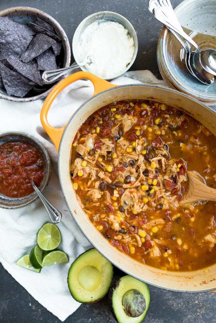 oval pot of chicken tortilla soup with black beans, corn, served with salsa, sour cream, lime, tortilla chips