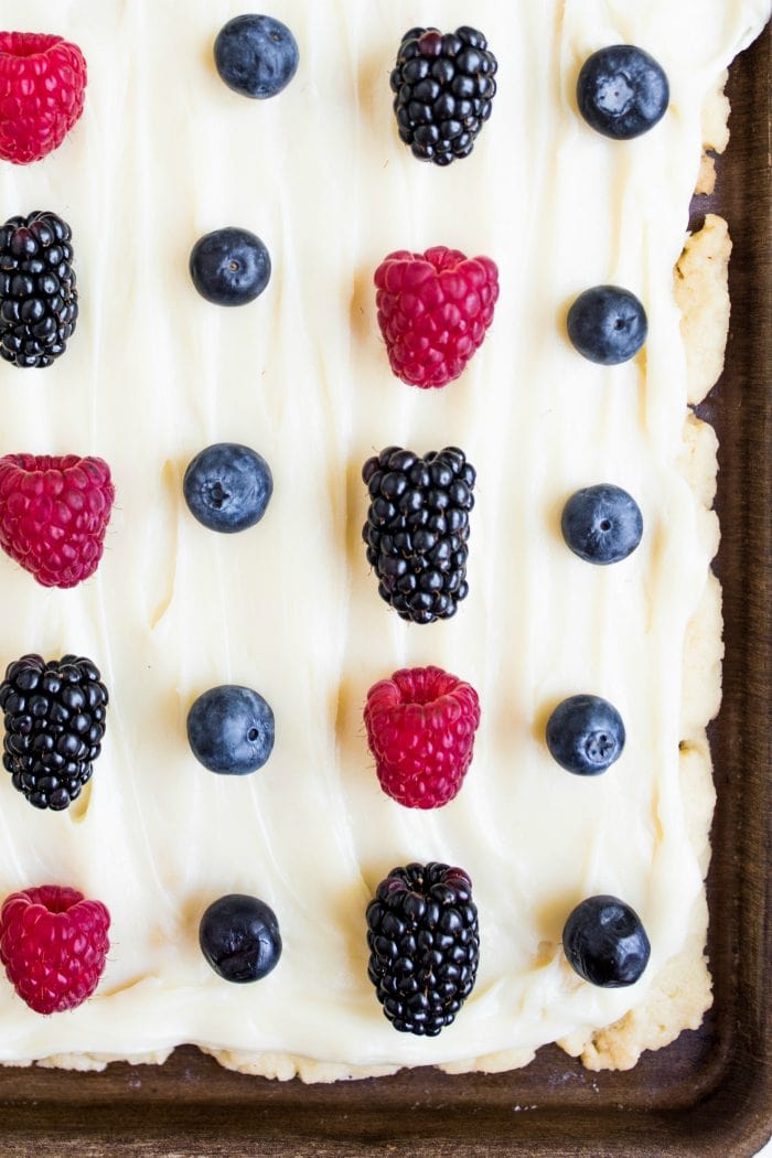 close up of sugar cookie bars in a pan, with fresh blueberries, blackberries, raspberries, and white frosting