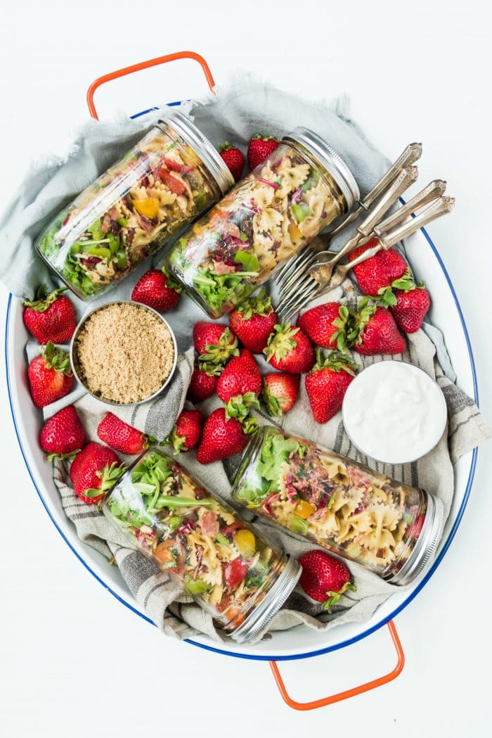 oval tray with 6 filled jars of pasta salad, with strawberries