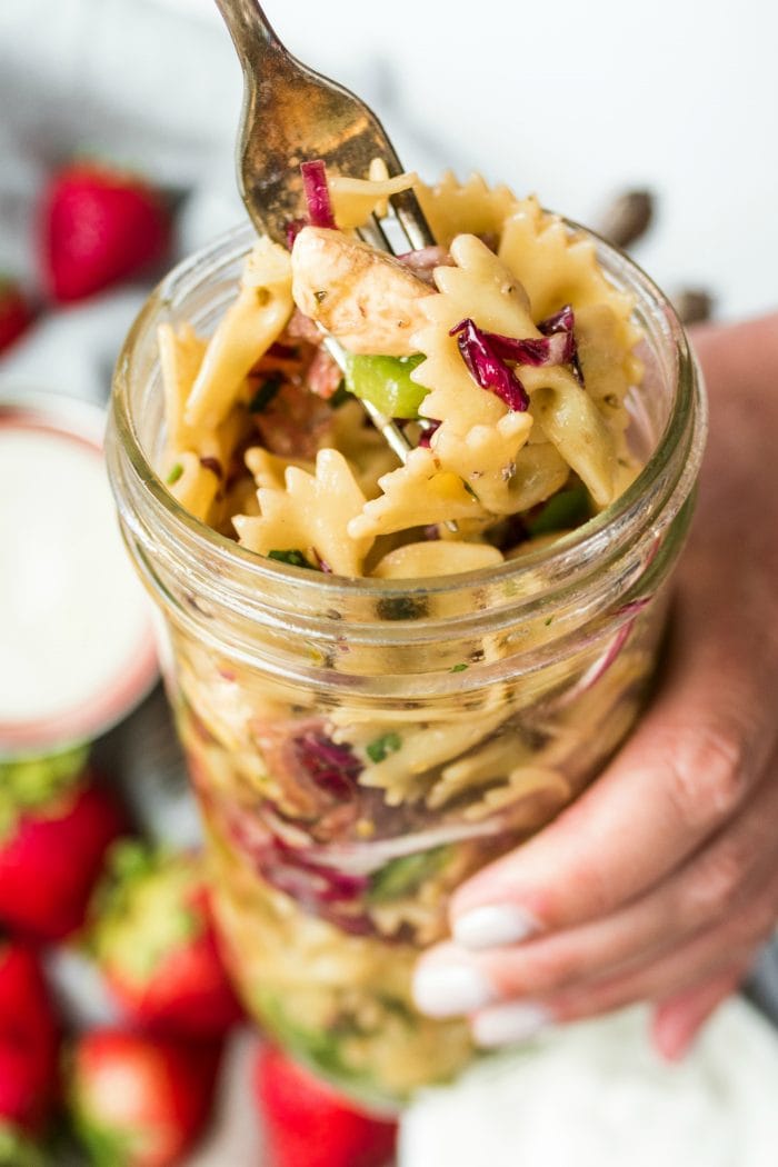 a fork filled with bowtie pasta salad, and holiding a jar of the salad