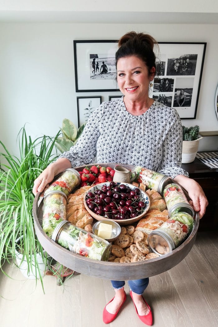 a woman holding an epic board filled with food (salad, cherries, strawberries, bread)