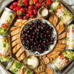 a round board with jars of salad, bread, strawberries, and a bowl of cherries