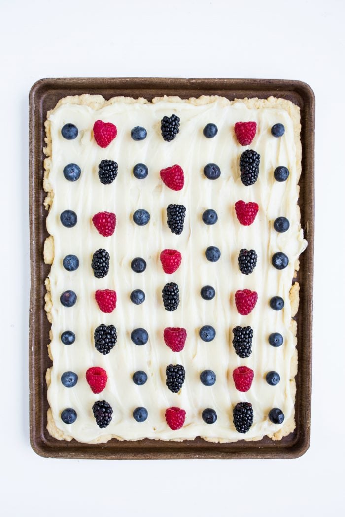 a baking pan of easy sugar cookie bars (crust) with white cream cheese frosting and fresh summer berries