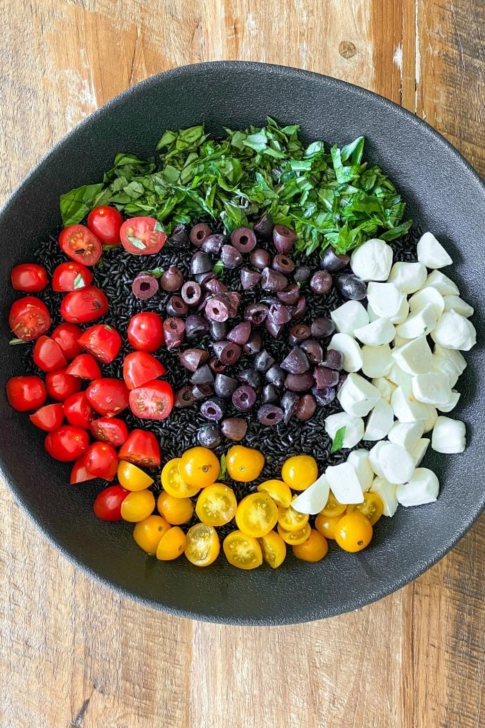 black bowl of black rice salad ingredients: forbidden rice, mozzarella cheese balls, cherry tomatoes, olives, and basil