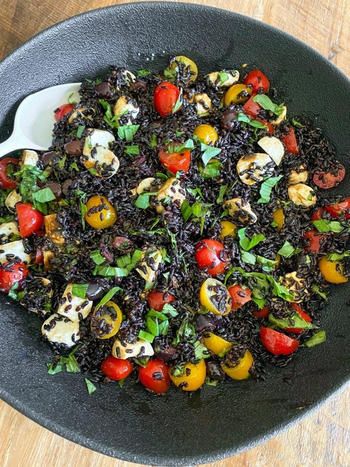 black bowl of black rice salad with colorful tomatoes, cheese, and basil