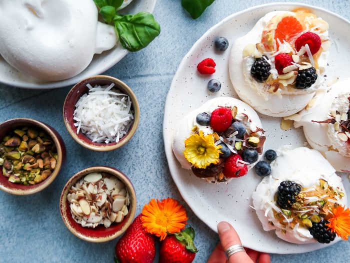 mini pavlovas on a plate with toppings like berries, nuts, and coconut