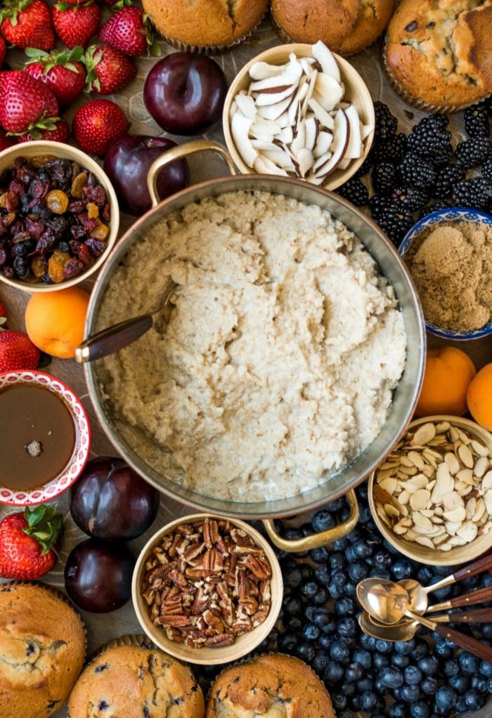 a pot of oatmeal, surrounded by small bowls of toppings and fresh fruit