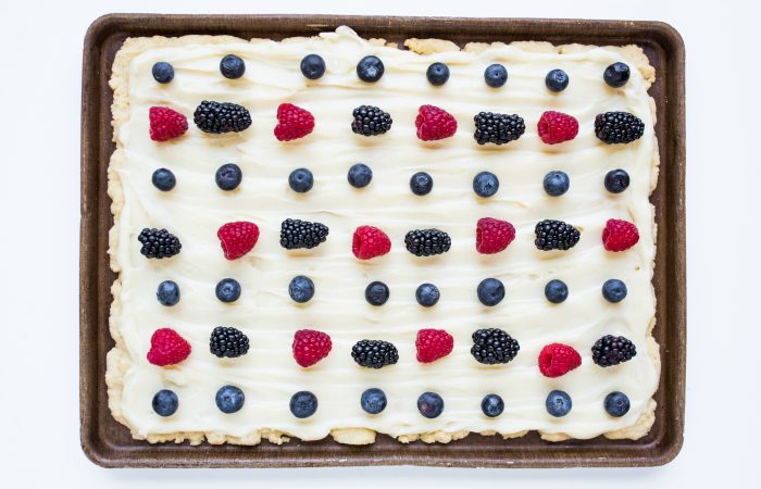 a baking sheet of sugar cookie bars with frosting and berries