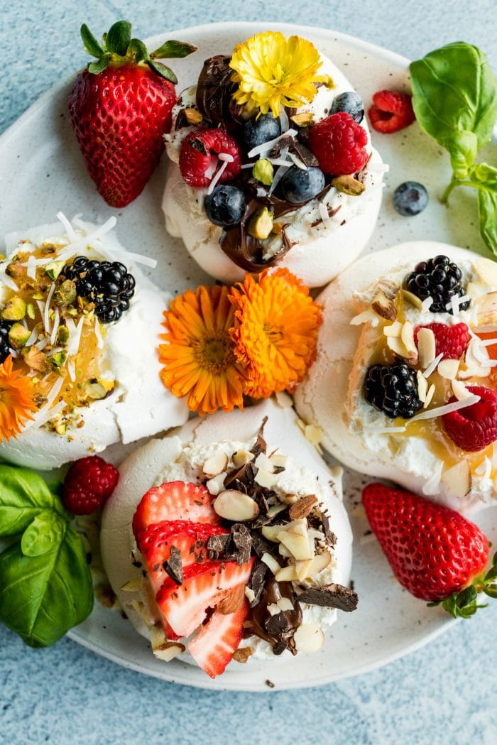 4 garnished mini pavlovas with berries, nuts, coconut, and ediblle flowers