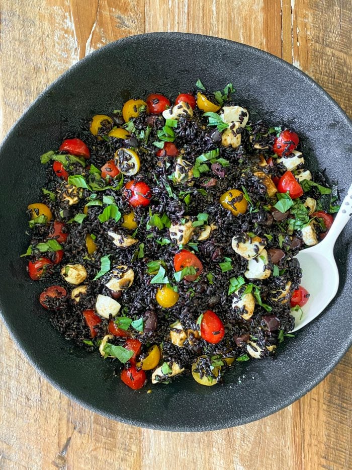 black bowl of black rice salad with cheese, tomatoes, and basil