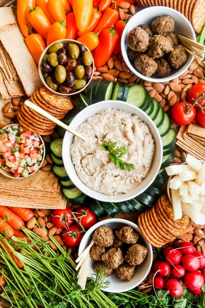 bowl of hummus on a platter with crackers, vegan meatballs, and veggies