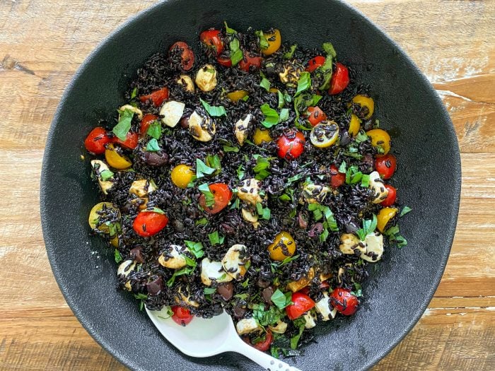 bowl of beautiful black rice salad with yellow and red tomatoes, cheese, and basil