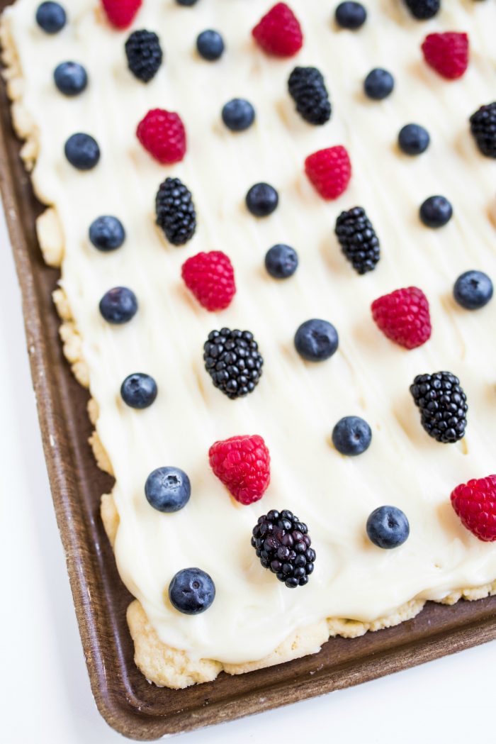 a baking sheet of sugar cookie bars with frosting and red and blue berries