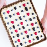 holding a baking sheet of sugar cookie bars with frosting and berries