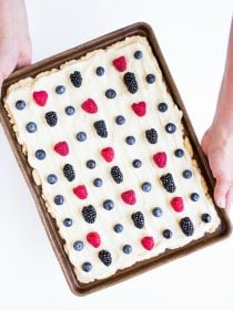 holding a baking sheet of sugar cookie bars with frosting and berries