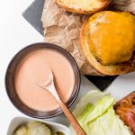 an open face cheeseburger with a small bowl of pink sauce