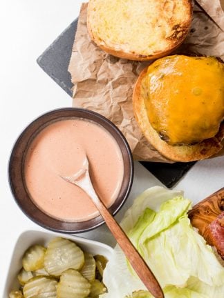 an open face cheeseburger with a small bowl of pink sauce