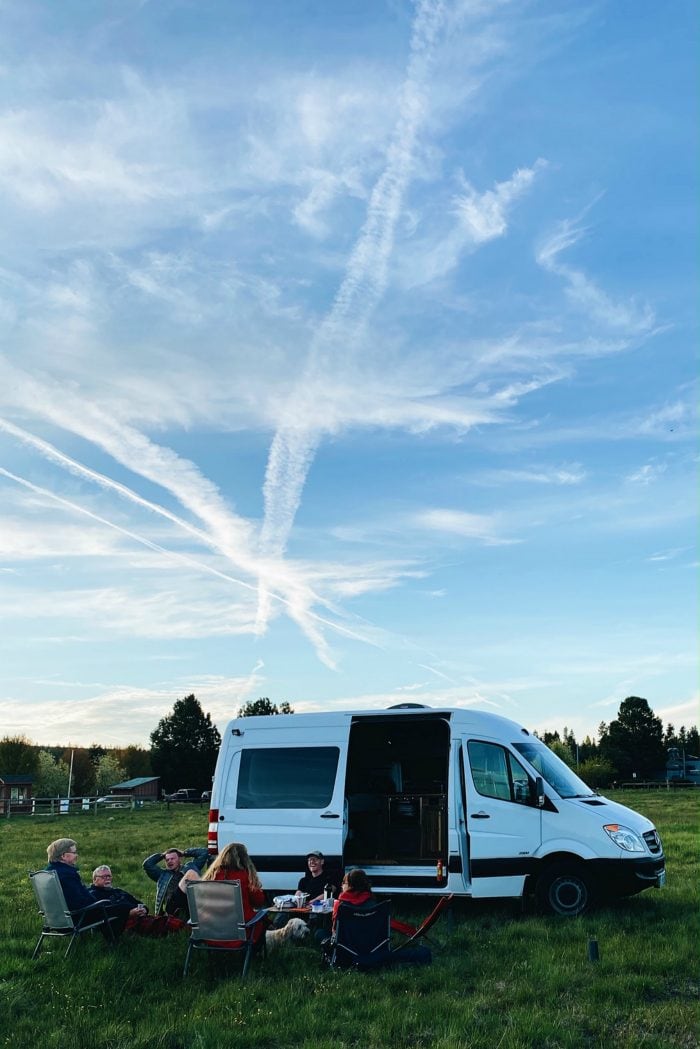 sprinter van in an open field with people sitting around