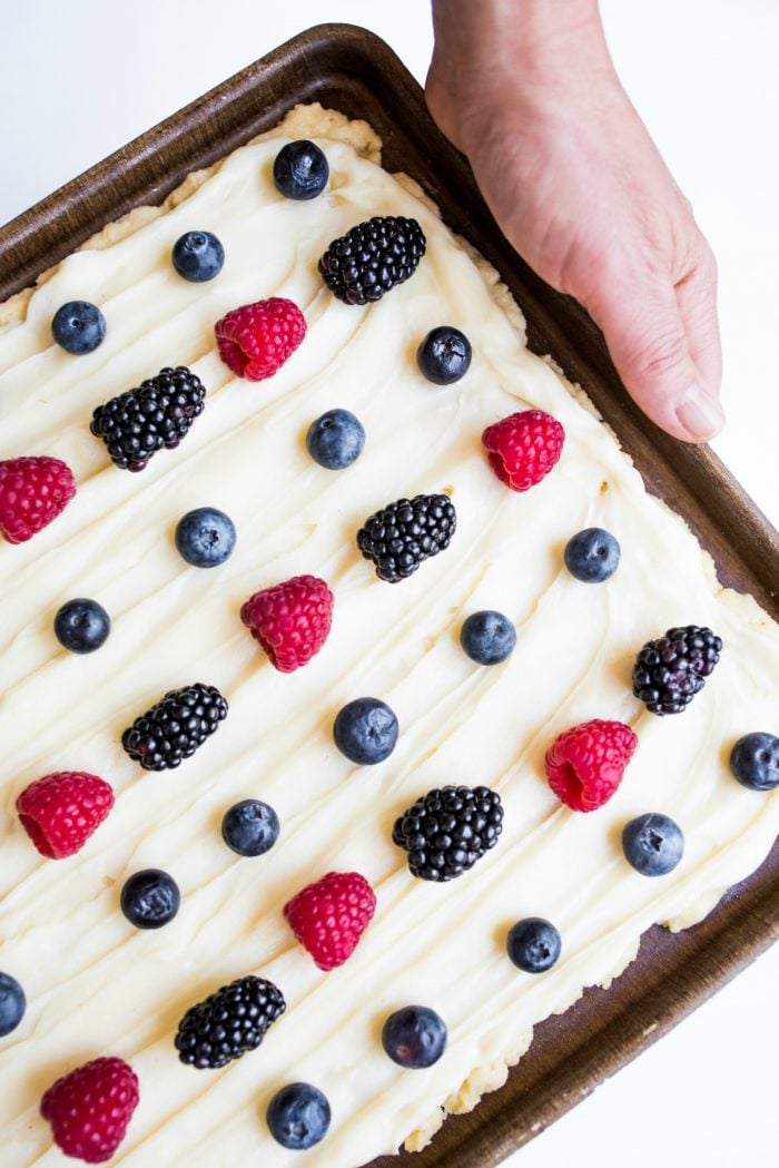 easy sugar cookie bars in a pan with white frosting and summer berries