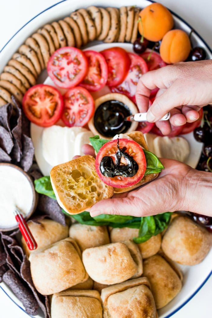 making a caprese slider, a hand drizzling balsamic glaze over the tomato