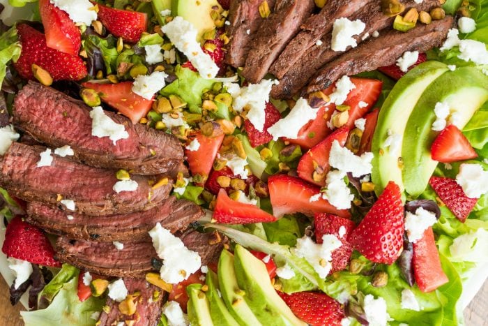 close up marinated balsamic steak slices on a bed of lettuce with strawberries, goat cheese, and avocado