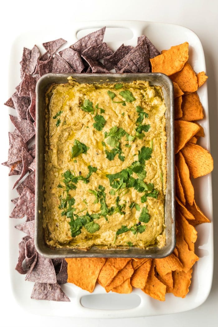 a pan of Corn Queso Dip served on a large white plate, with chips around the outside